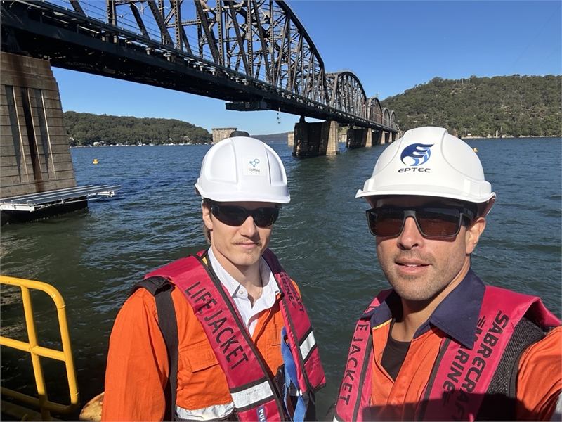 Two iottag engineers in hard hats and life jackets working beside a rail bridge over water