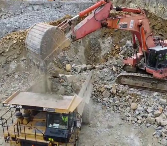 Excavator loading blasted rock into a haul truck on an open-cut mine bench