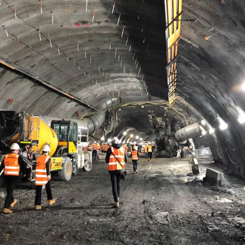 Crews, a loader and a concrete truck working together along an excavated tunnel heading