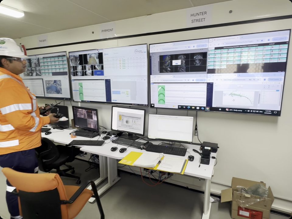 Operator monitoring live asset dashboards across a wall of screens in a site control room